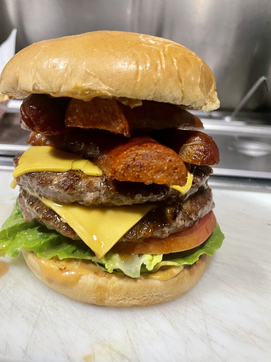 A double cheeseburger on a brioche bun with lettuce and tomato, topped with sliced grilled sausage